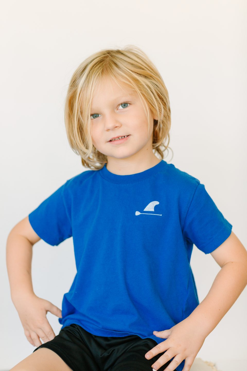 Smiling boy in a blue T-shirt with his hands on his hips in the studio