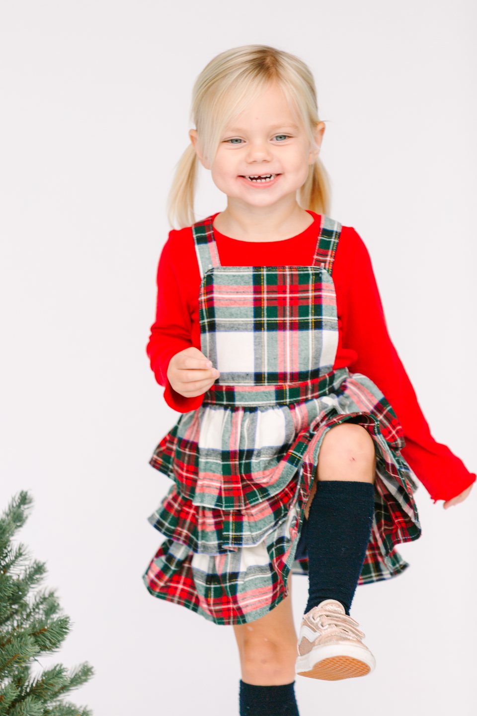 Child in a plaid holiday dress lifting one knee in the studio