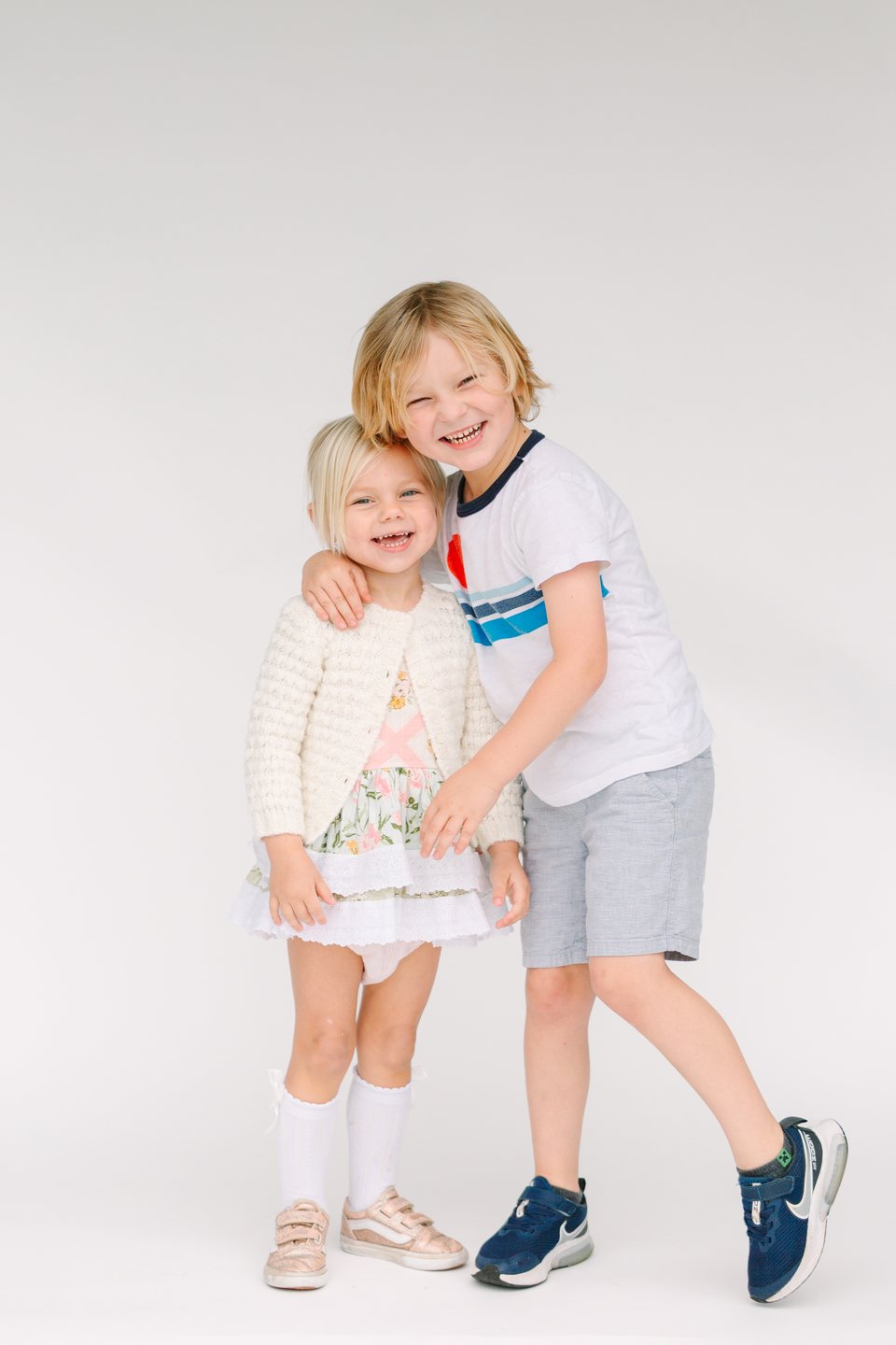 A boy and a little girl hugging and laughing in a white studio
