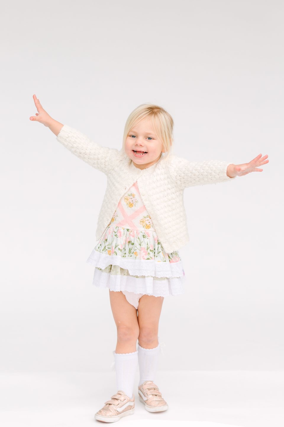 Toddler in a cream cardigan flinging her arms wide in the studio