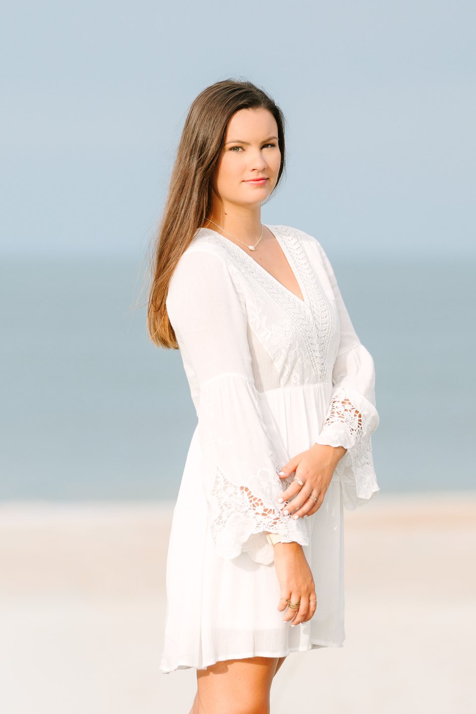 Young woman in a white dress standing on the beach with the ocean behind her