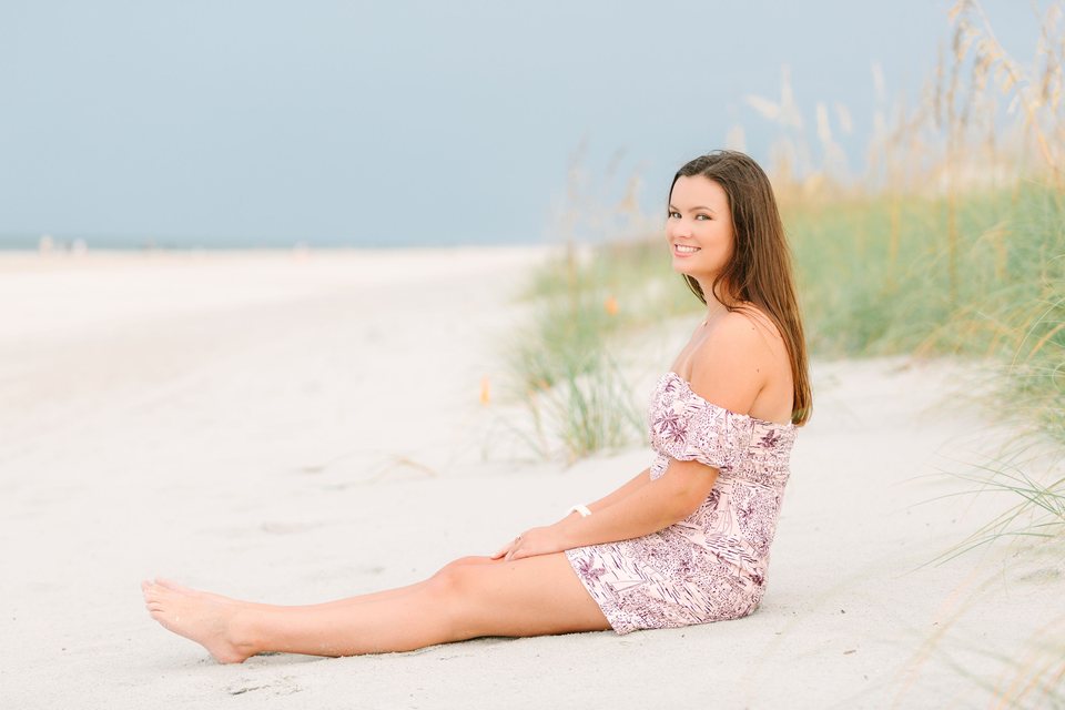 Young woman sitting in pale sand beside beach grasses