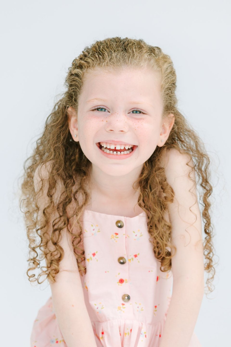 Laughing child with curly hair in a pale pink dress