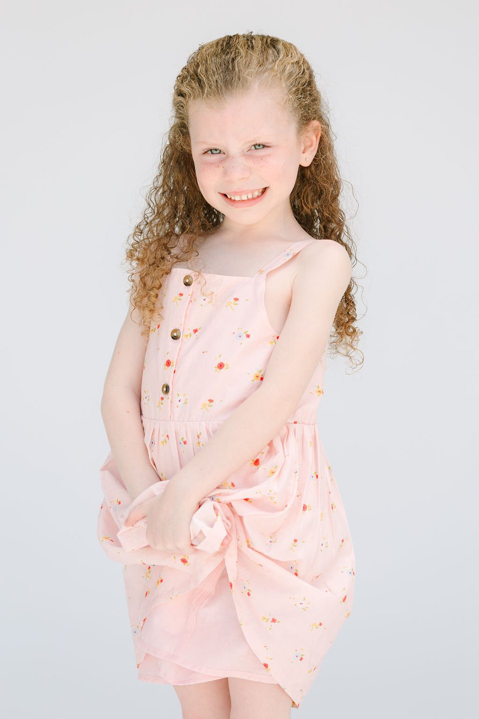 Girl with curly hair in a pink dress smiling in the studio