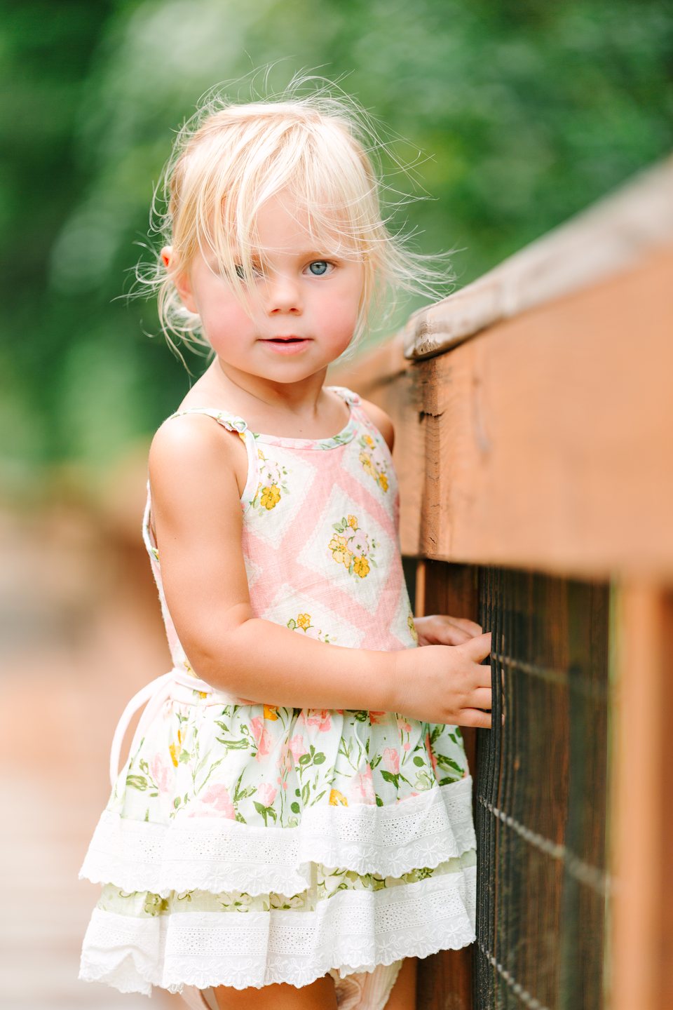 Toddler in a floral sundress leaning on a wooden railing