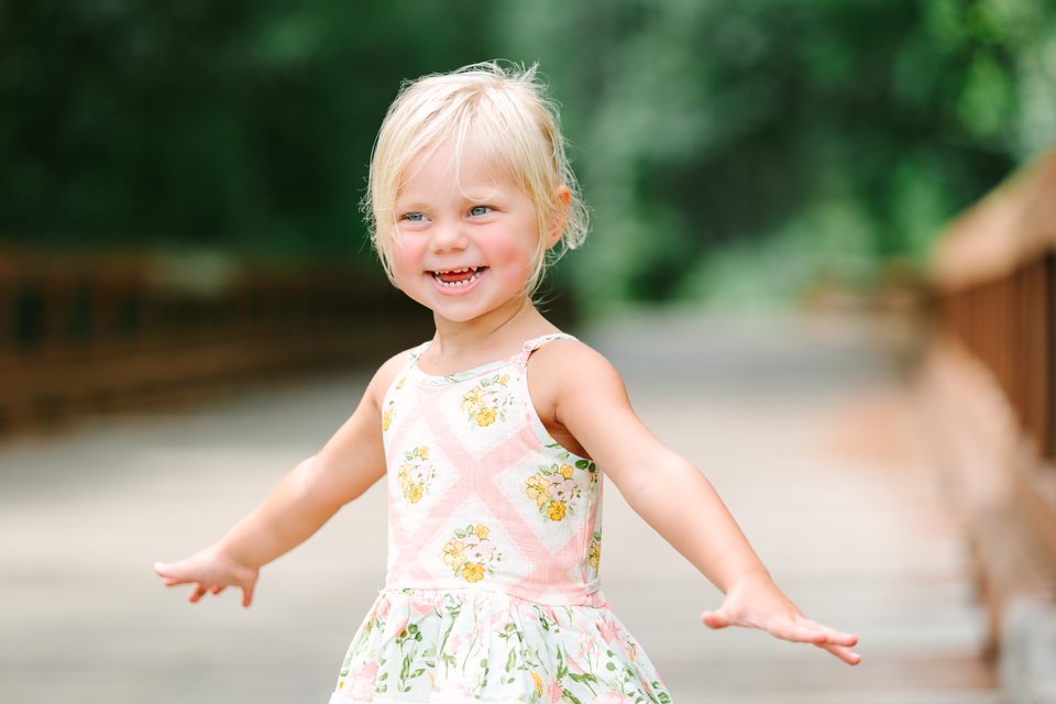 Toddler in a floral sundress running with her arms out on a path