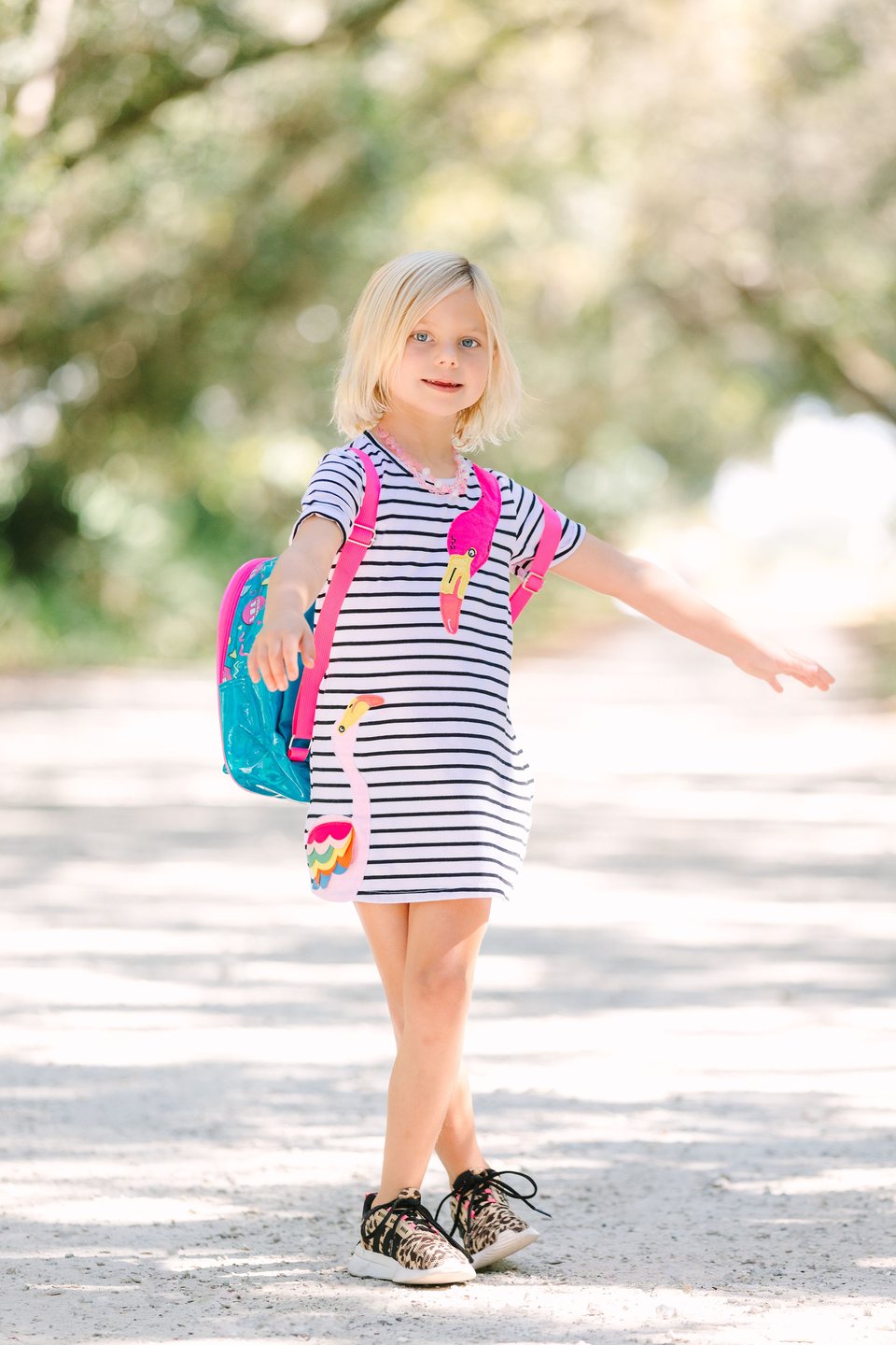 Child in a striped dress with arms out on a sunlit path