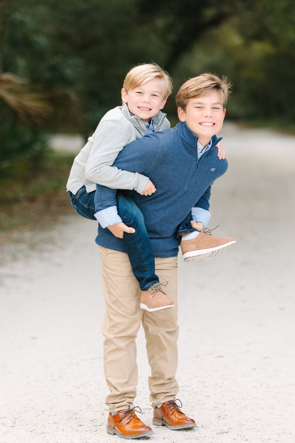 Two brothers laughing during a piggyback ride on a sandy path