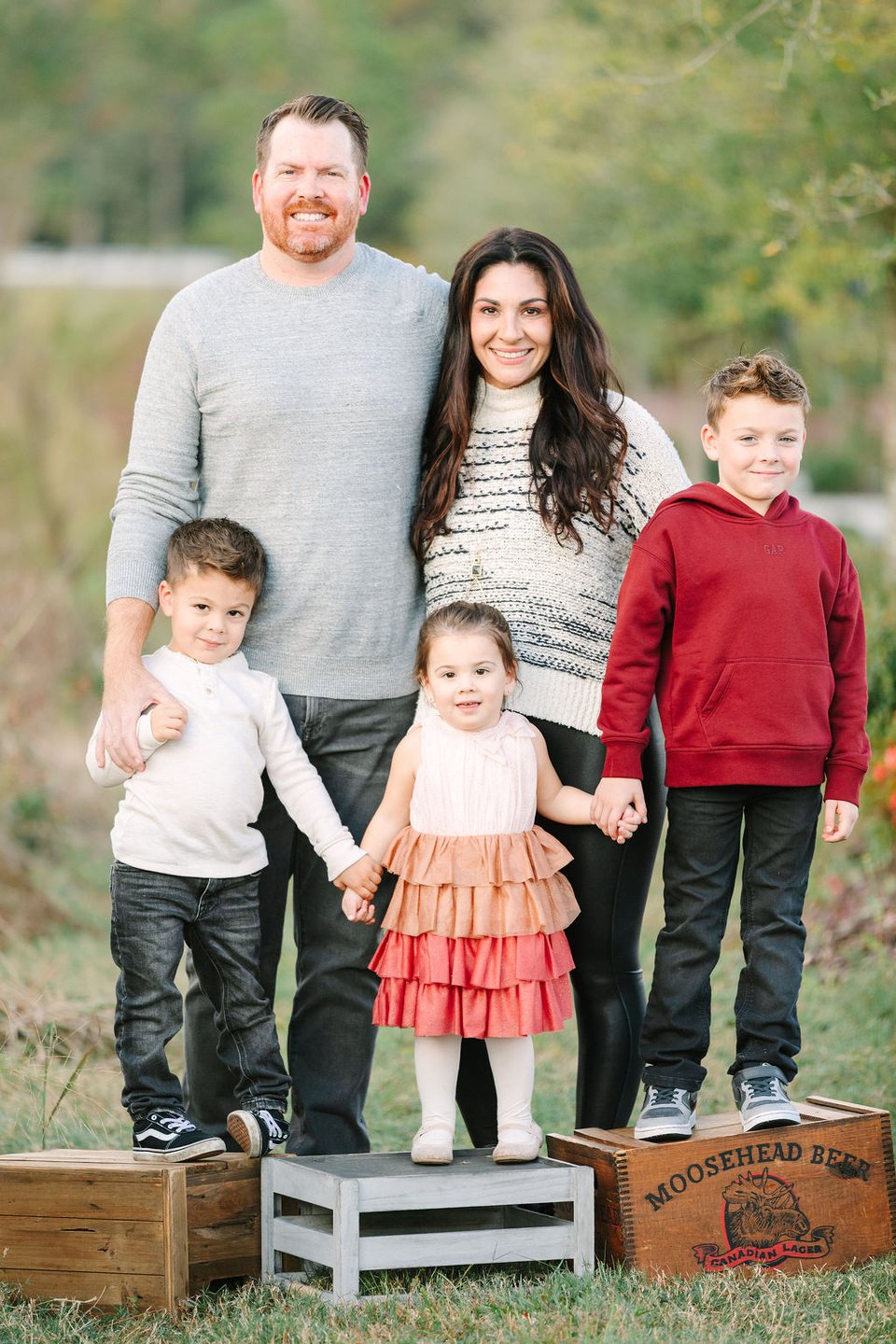 Family of five with young children standing on wooden crates in tall grass