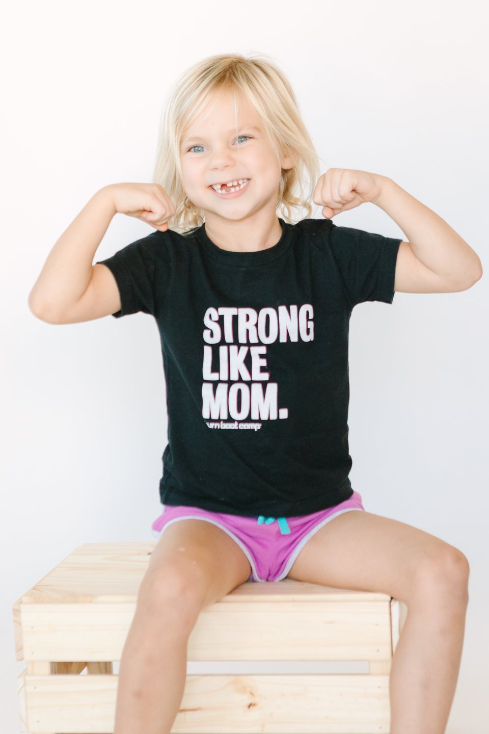 Child in a black tee flexing her arms and grinning in the studio