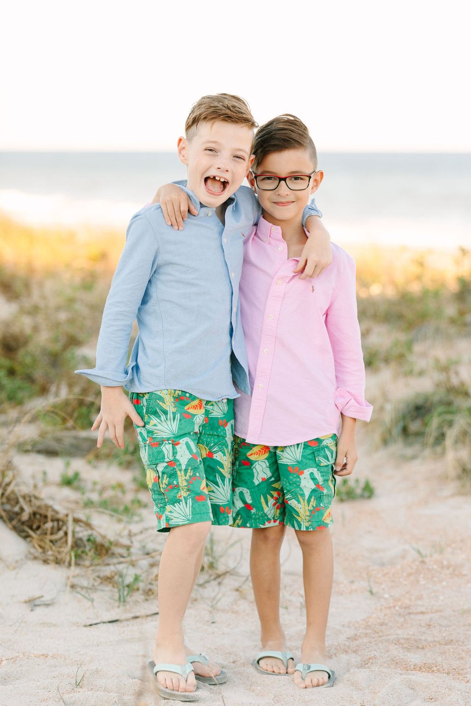 Two brothers in pink and blue shirts standing in the dunes