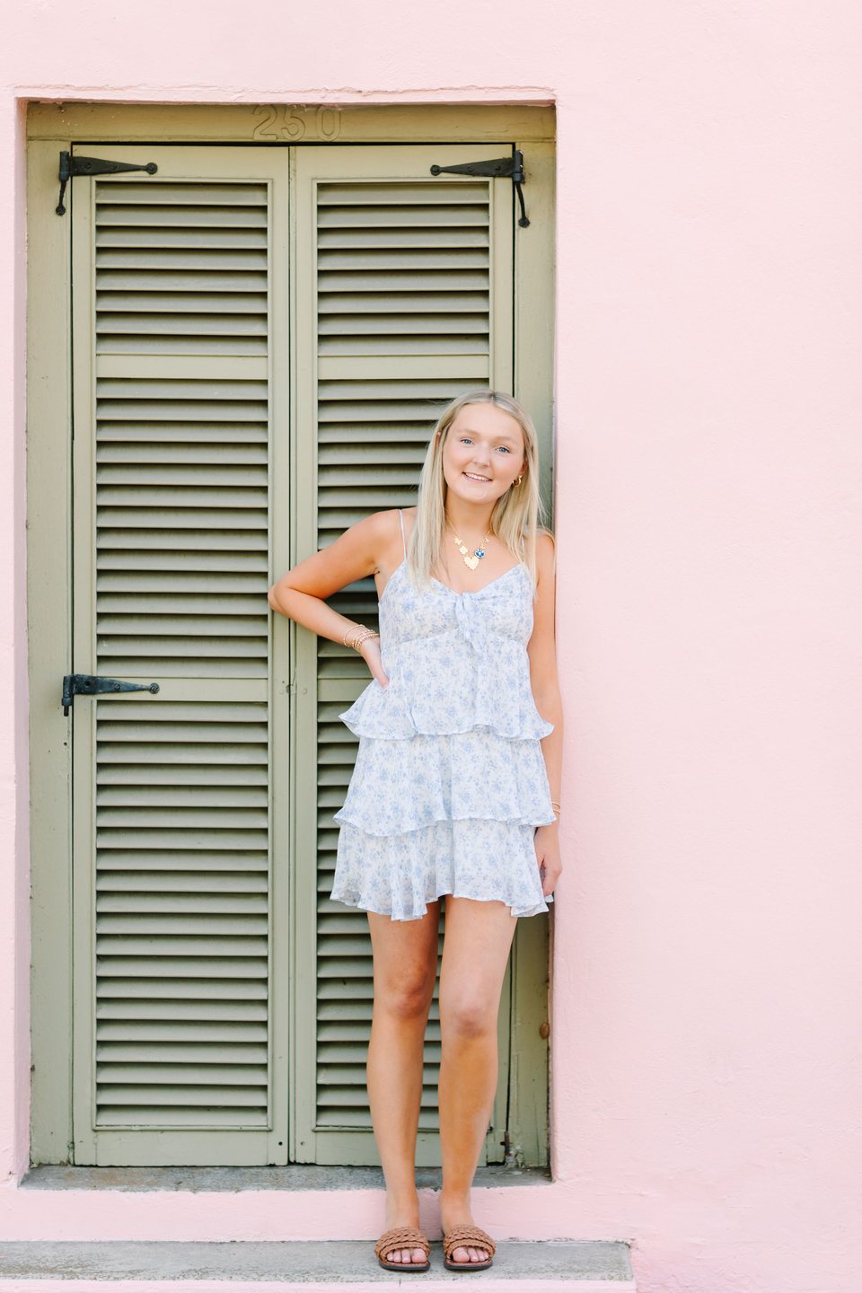Young woman in a floral outfit beside a pink wall and green shutters