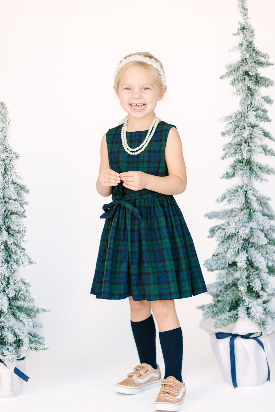Child in a green plaid dress and pearls between snowy trees