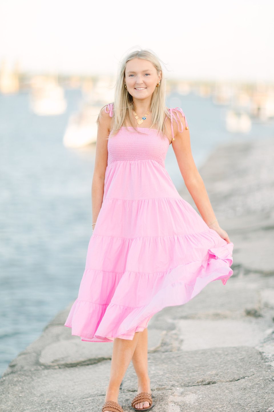 Young woman in a long pink dress walking along the rocks by the water