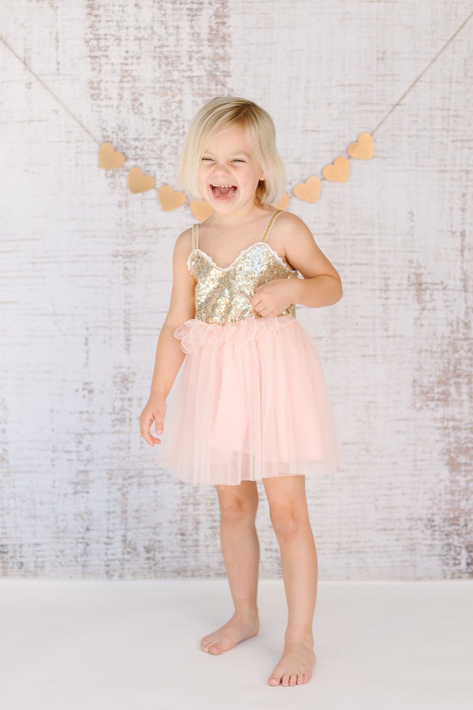 Child in a sparkly pink dress laughing in a studio