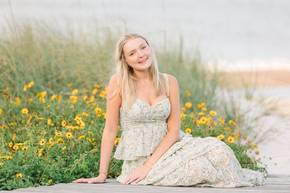 Young woman seated beside yellow flowers and beach grasses