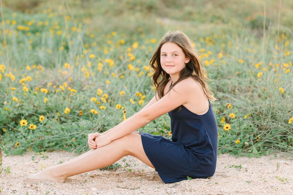 Young woman in a navy dress sitting among yellow wildflowers