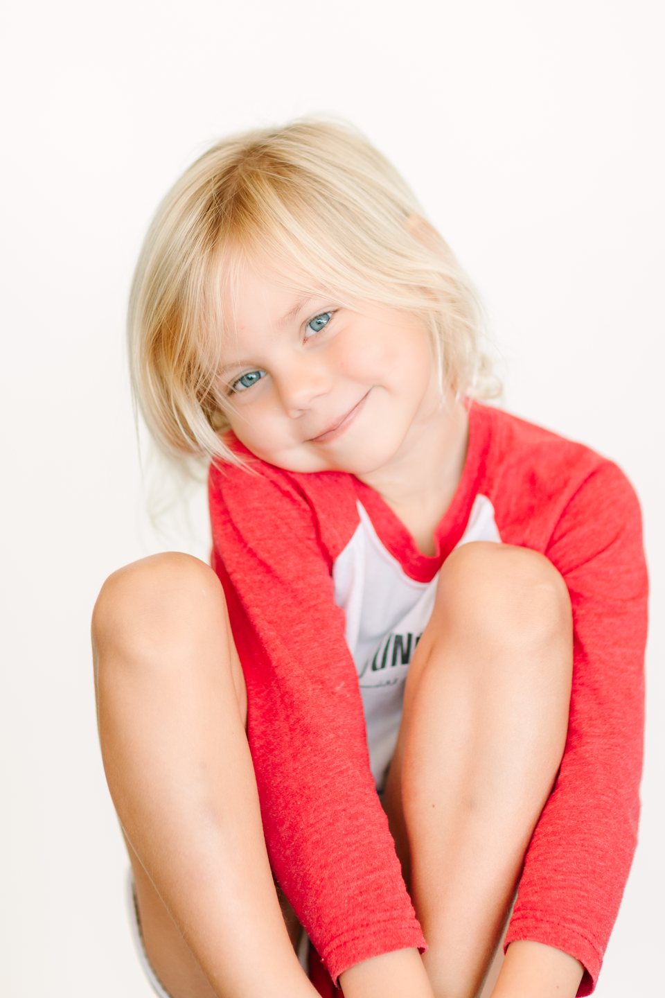 Small boy in a red and white shirt tilting his head in the studio