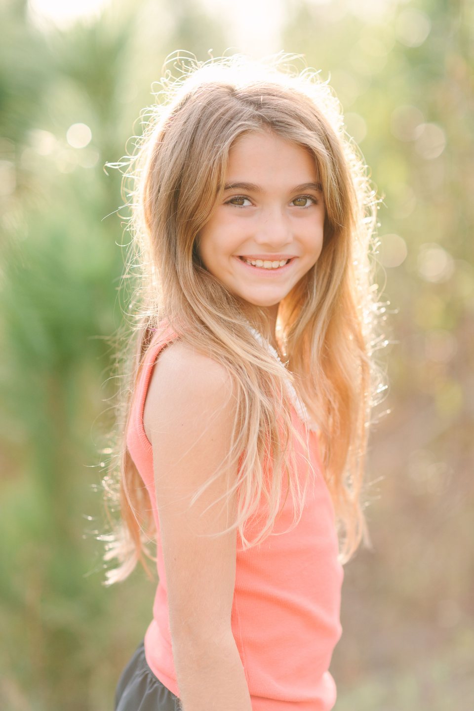 Smiling girl with long hair in a coral top, backlit by evening sun