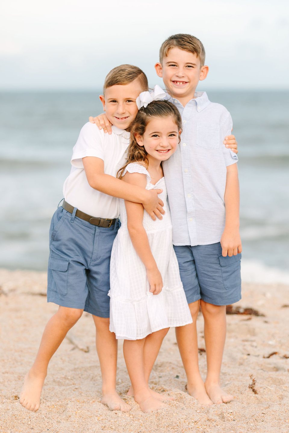 Two boys and a girl hugging and smiling on the beach
