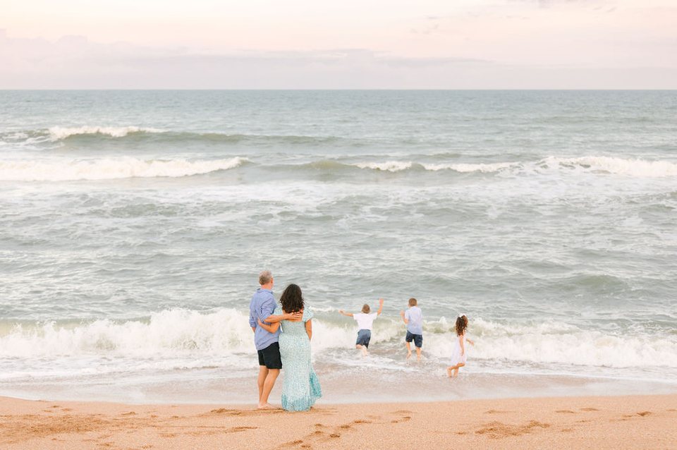 Family walking into the waves at dusk, seen from behind