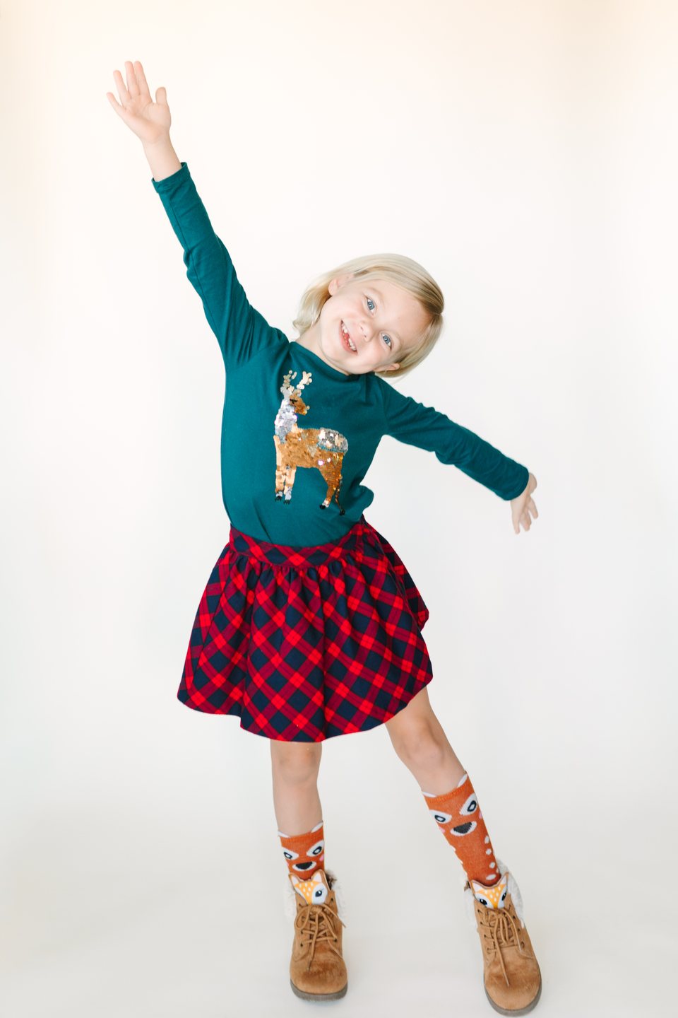 Child in a reindeer sweater with one arm raised in the studio