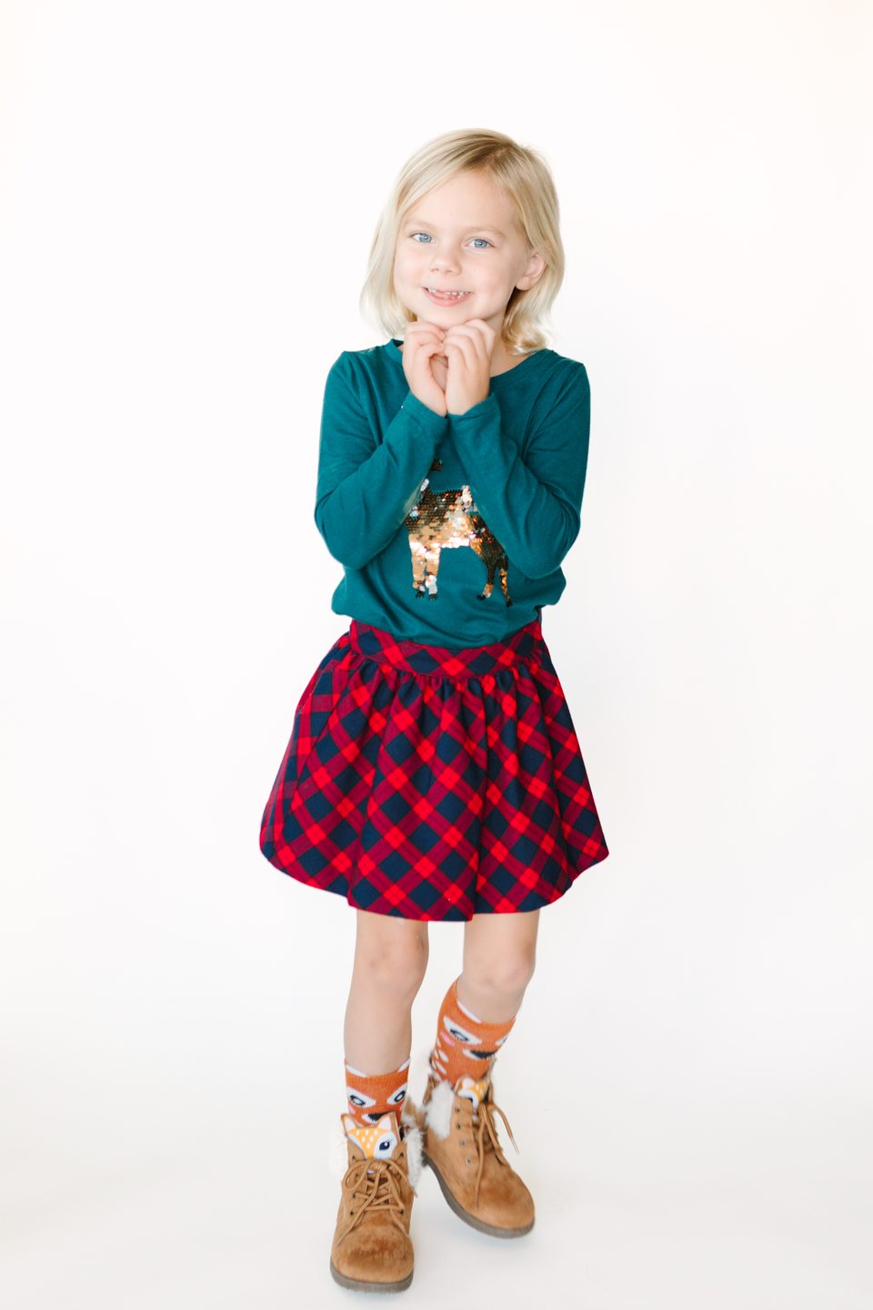 Girl in a green sweater and red plaid skirt with her hands clasped in the studio