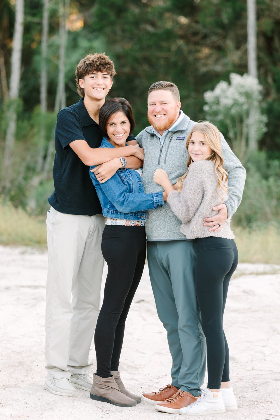Family of four hugging on a sandy path