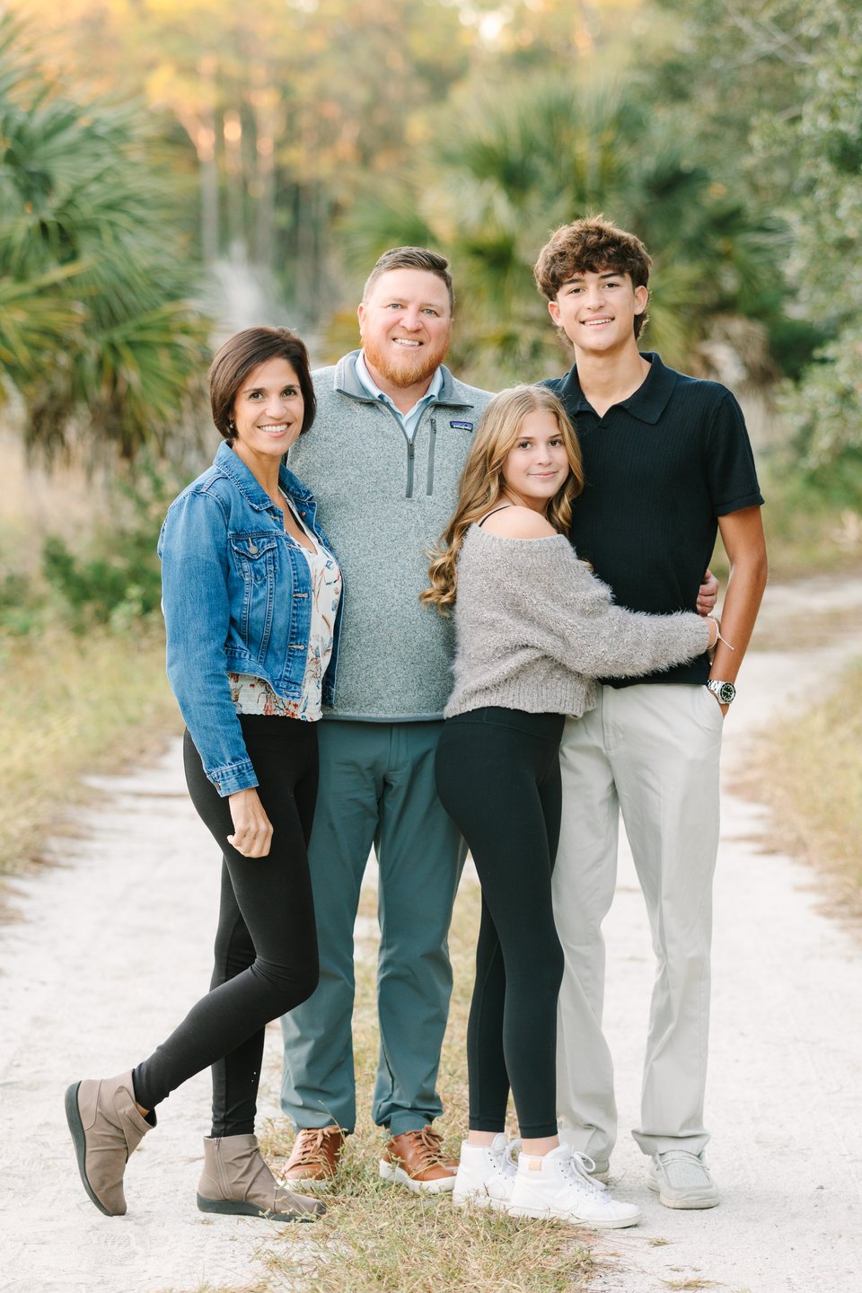 Family of four standing close together on a sandy path