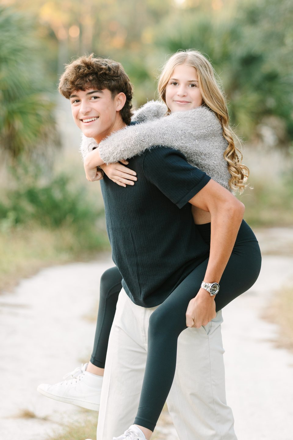 Brother giving his sister a piggyback ride on a sandy path