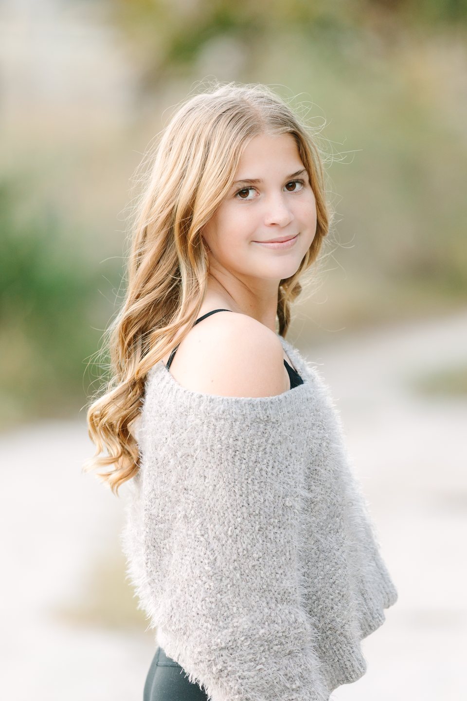 Teen in a gray sweater looking over her shoulder on a sandy path