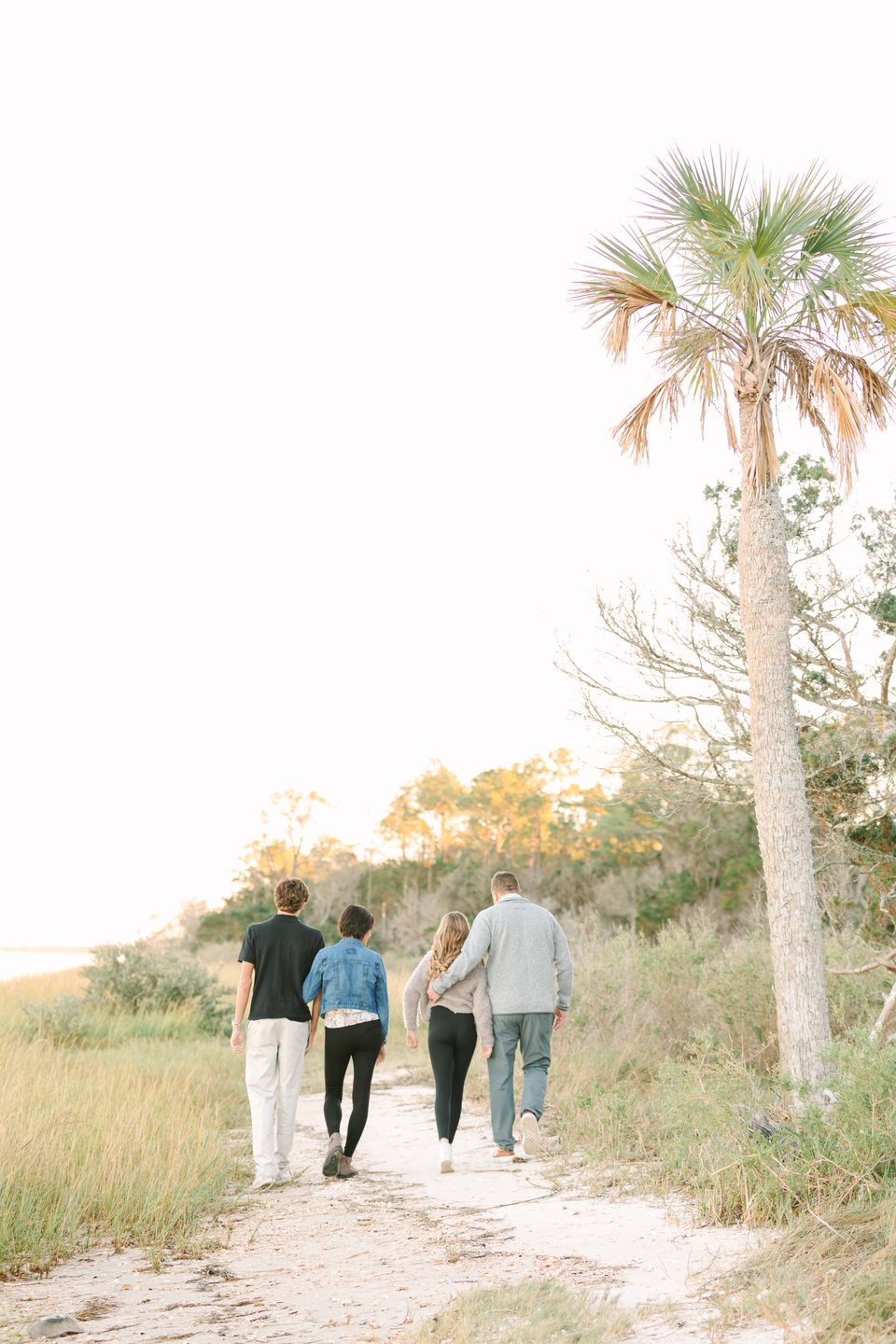 Family of four walking away down a sandy path beside a palm tree