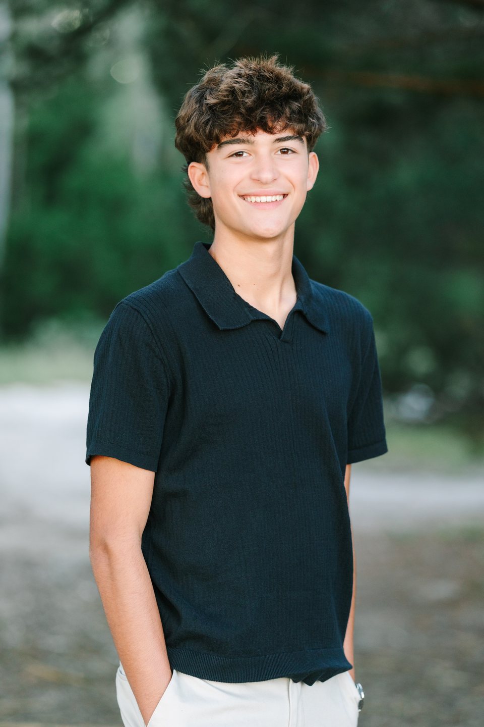 Smiling teenage boy in a navy polo standing on a tree-lined path