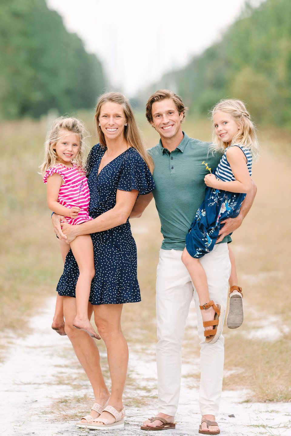 Family of four smiling on a sandy path, each parent holding a little girl