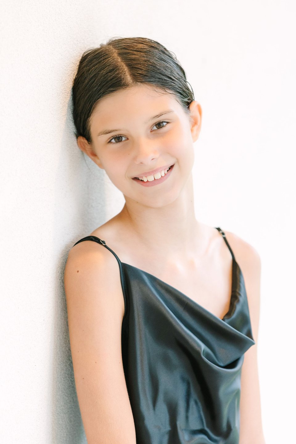 Child in a black dress smiling against a pale wall