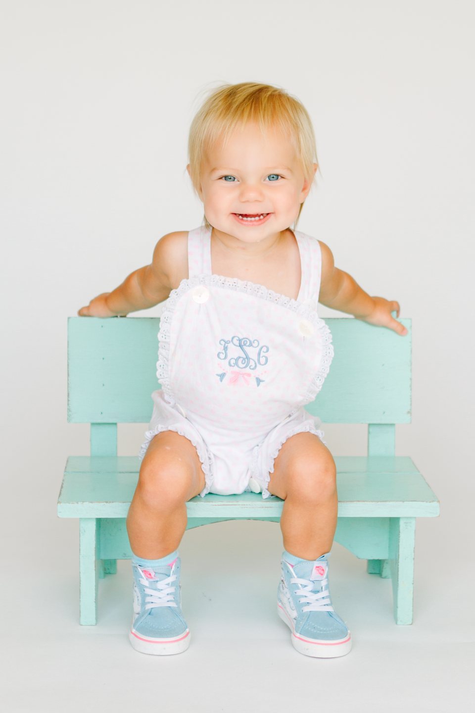 Baby in a monogrammed romper on a mint bench