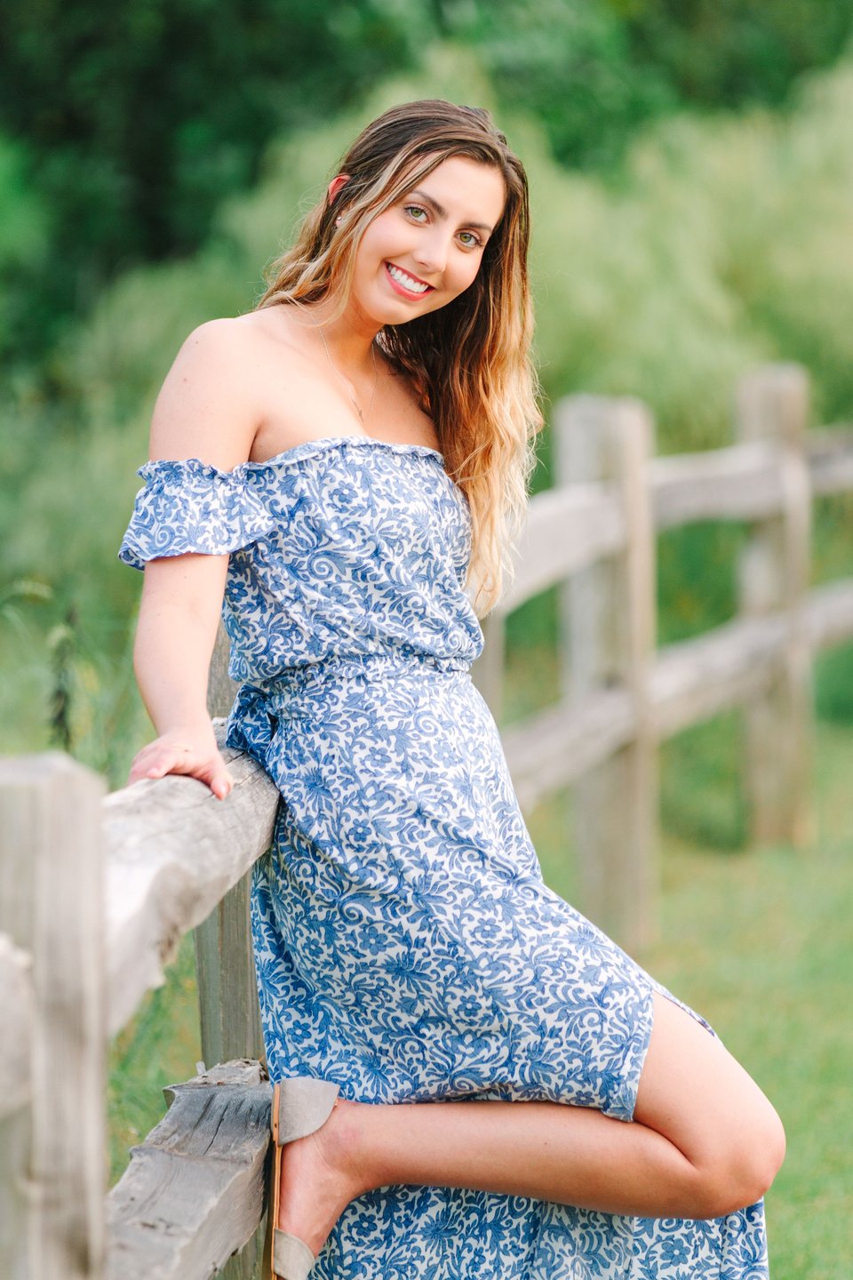 Young woman in a blue floral dress leaning on a wooden fence