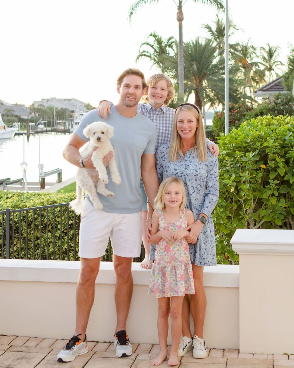 Family of four holding a small white dog on a waterfront patio