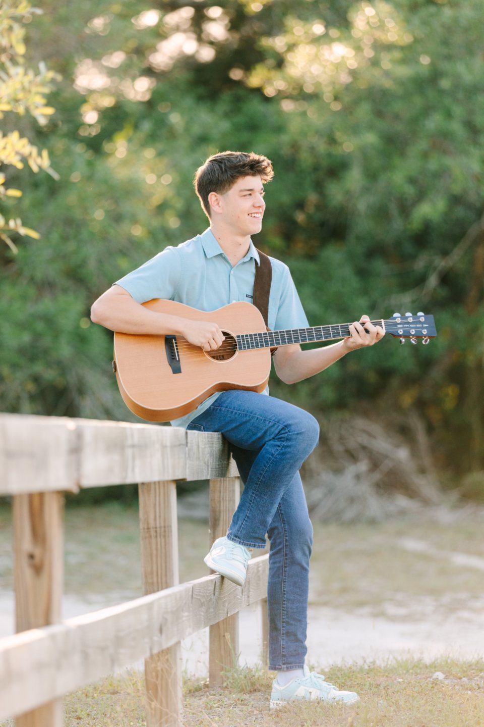 Teenage boy playing guitar while sitting on a wooden fence