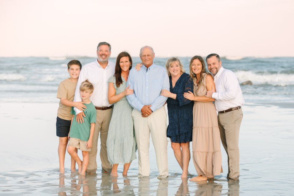 Extended family standing together in the shallows at sunset