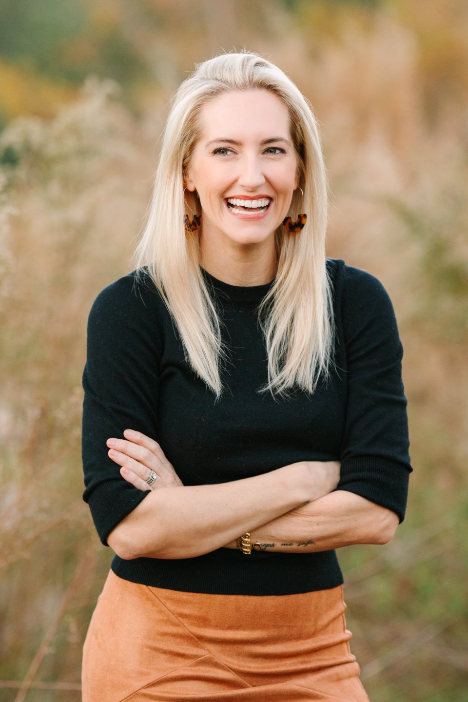 Laughing woman in a black sweater with her arms crossed among tall golden grass