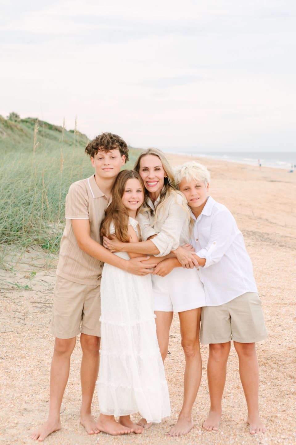 A woman and three children hugging on the beach beside the dunes