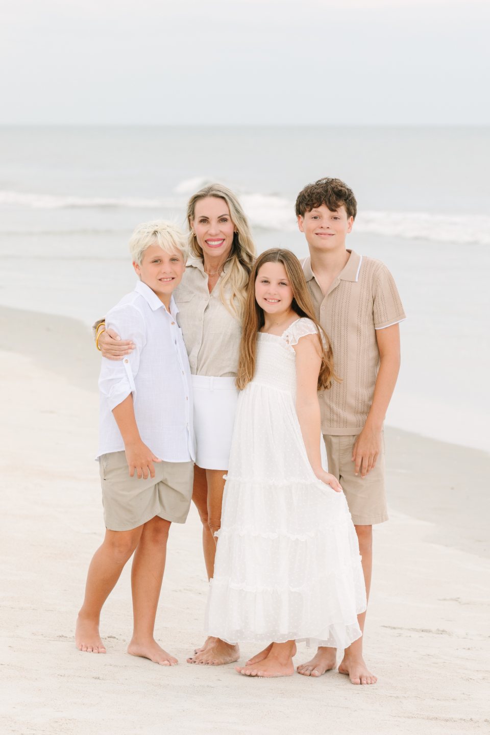 A woman and three children standing close together on the beach