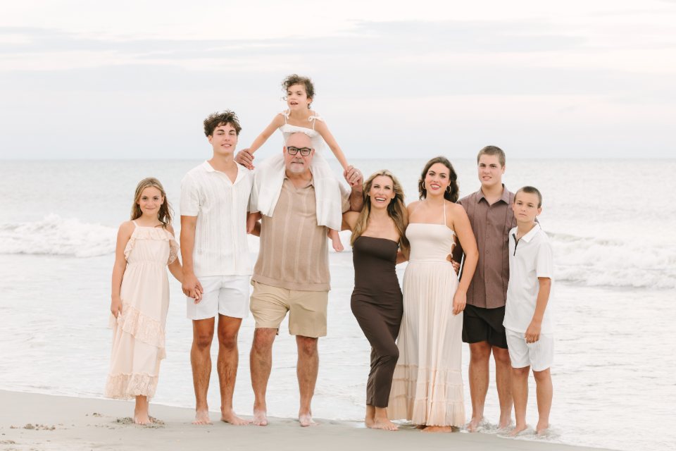 Extended family at the water's edge with a child lifted high in the middle