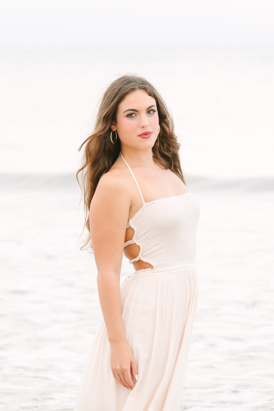 Young woman in a cream dress posing at the beach with the ocean behind her