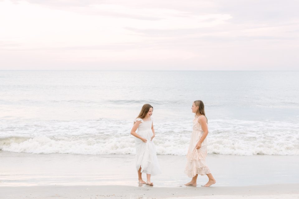Two girls in white dresses playing in the surf at dusk