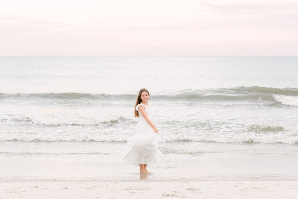 Young woman in a white dress walking through the shallow surf at dusk