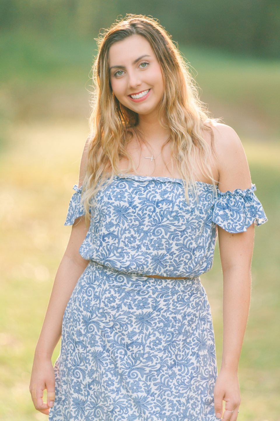 Smiling young woman in a blue off-the-shoulder dress in a sunlit field